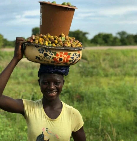 A black woman carryring items on top of her head. The Ajike Shea Centre is a social enterprise which was established to empower rural women in Ghana who are the backbones of their families.
